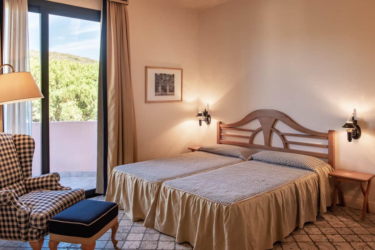 Une chambre avec deux lits, une chaise, une table et une vue sur la verdure.