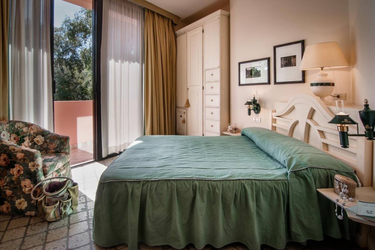 Une chambre d’hôtel avec un lit, une chaise, une armoire, une table de chevet et une fenêtre avec des rideaux.