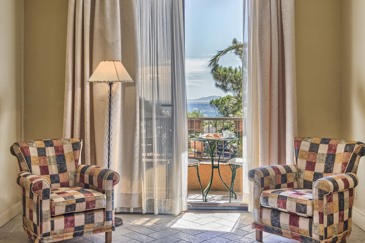 A room with two armchairs and a table, a lamp, and a view of the sea through sheer curtains.