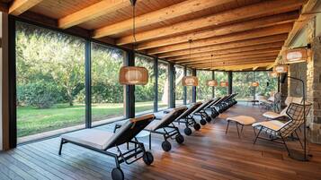 A covered outdoor area with wooden flooring, large windows, and several massage chairs.