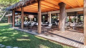 An outdoor patio with wooden tables and chairs, surrounded by stone pillars and a thatched roof. - Roccamare Resort - Hotel Casa di Ponente (Castiglione della Pescaia)