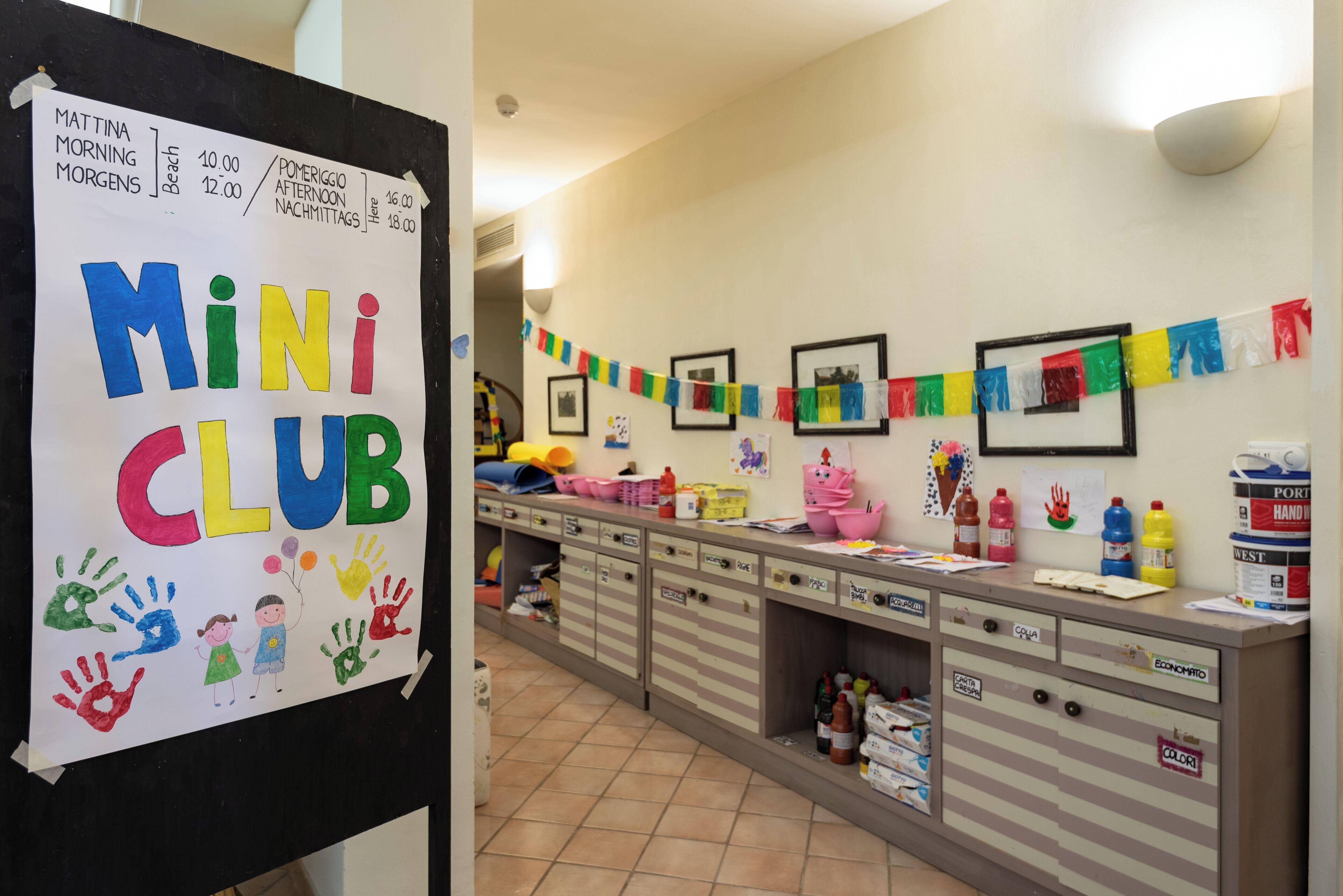 A classroom with a bulletin board displaying a schedule and a colorful 'Mini Club' sign.