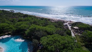 An aerial view of a coastal area with a beach, a swimming pool, and dense greenery. - Roccamare Resort - Hotel Casa di Ponente (Castiglione della Pescaia)