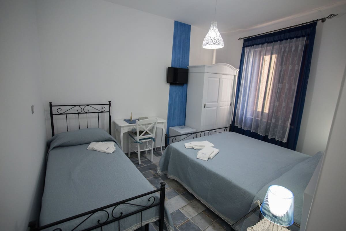 Una habitación pequeña y limpia con dos camas individuales, un escritorio, una silla, un armario y un televisor montado en la pared.