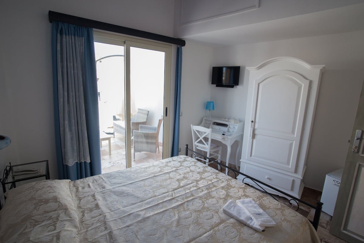 Una habitación de hotel con cama, escritorio, televisor y balcón con sillas.