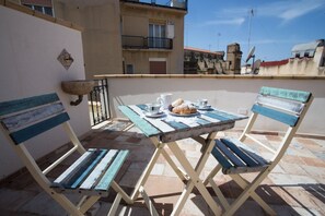 A small outdoor seating area with a table and two chairs, a stone sink, and a view of a building with balconies. - Coraje Room & Breakfast (Sciacca)