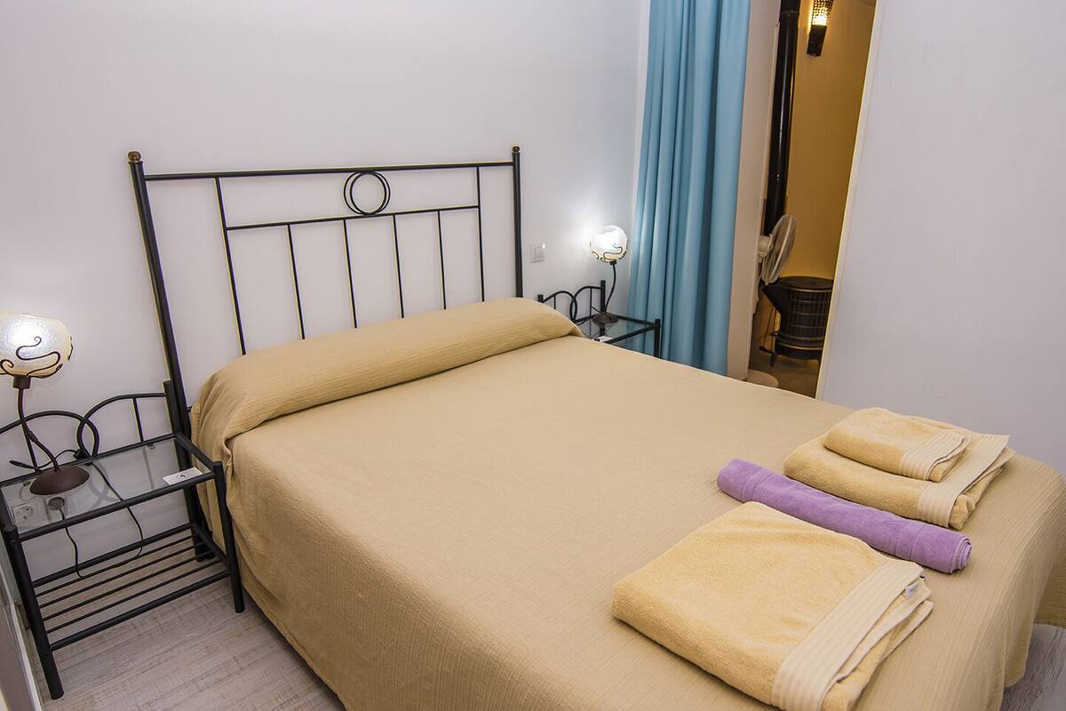 A neatly made bed with a beige bedspread and two towels, a bedside table with a lamp, and a mirror on the wall.