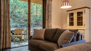 Ein gemütlicher Wohnbereich mit einer Couch, einem Esstisch mit Stühlen und Blick auf einen Wald durch eine Glastür.