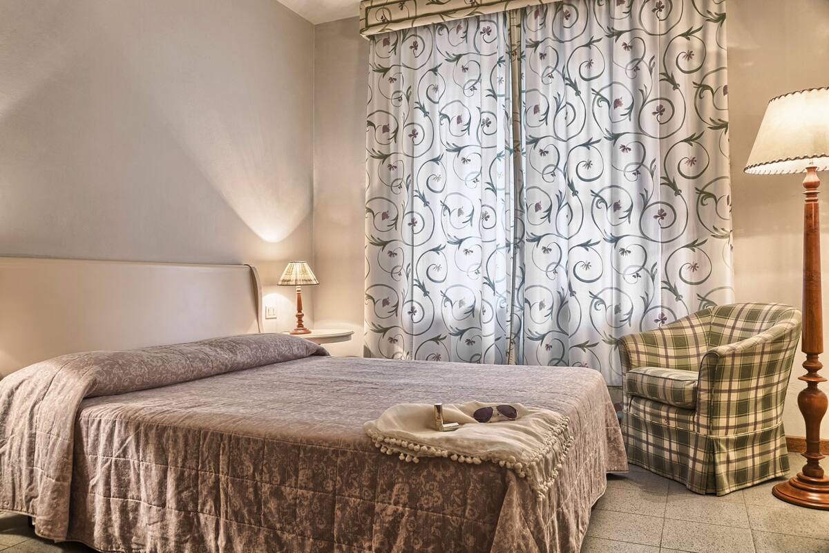 Una camera da letto con un letto, una sedia, una lampada e delle tende.