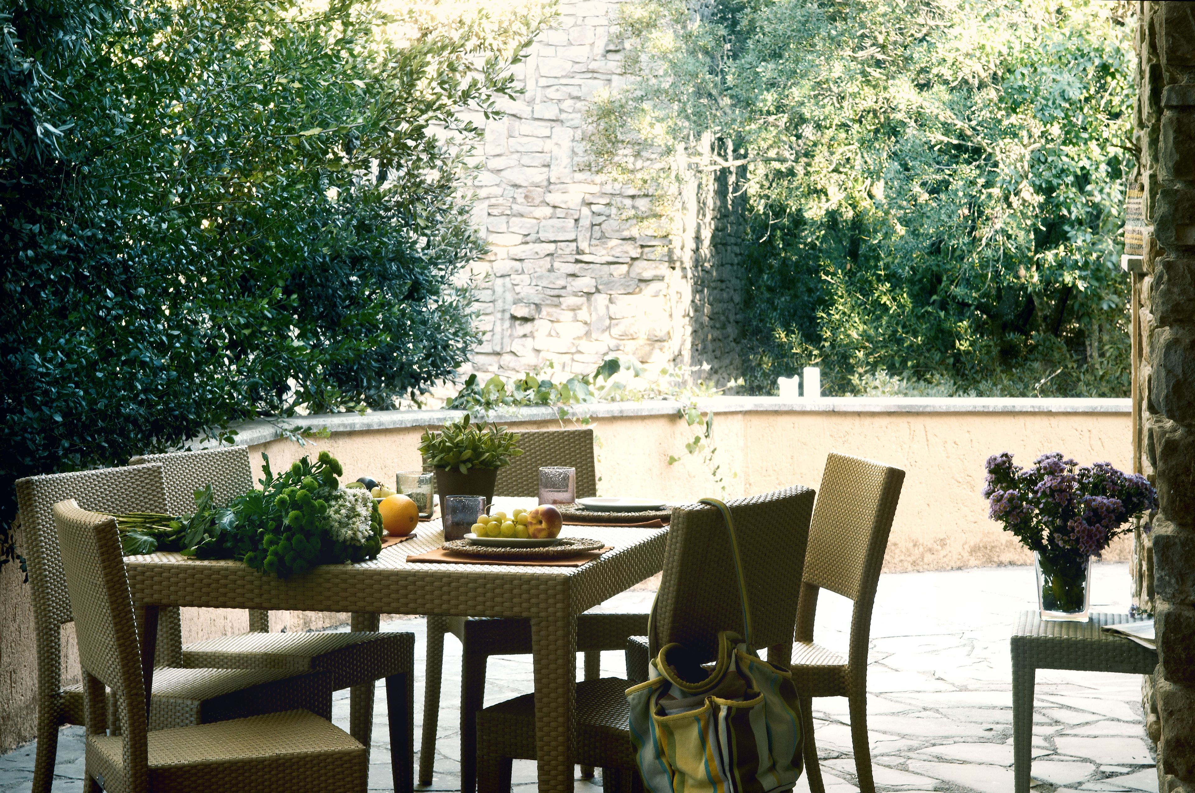 Eine Terrasse im Freien mit Korbmöbeln, einer Steinmauer und üppigem Grün.