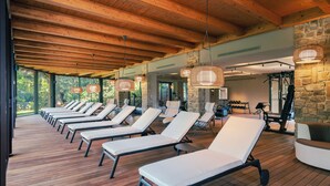 Ein sonnendurchfluteter Raum mit Holzböden und -decke, ausgestattet mit Liegestühlen und Fitnessgeräten.