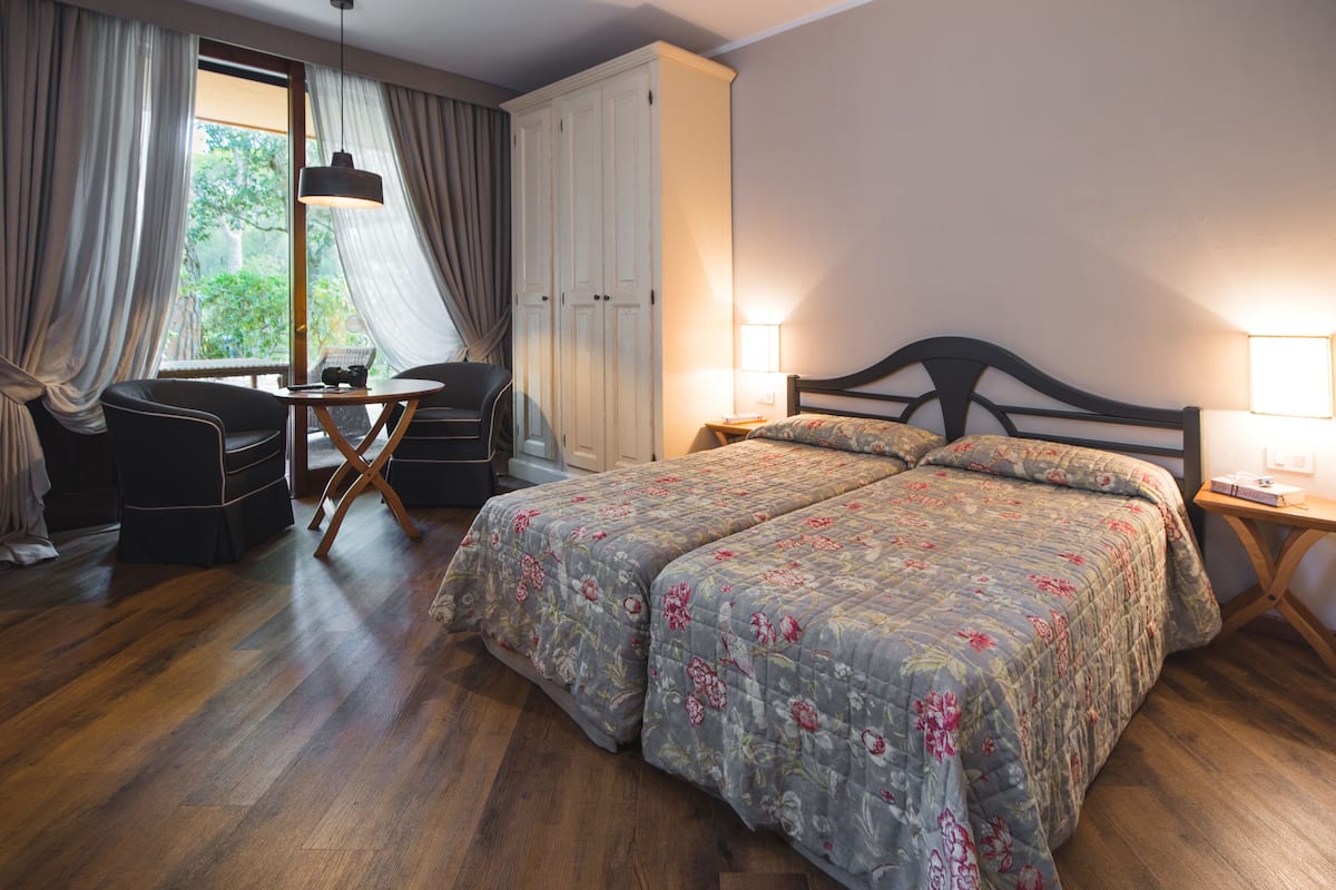 Una camera d'albergo con un letto grande, una scrivania con sedia, un armadio e una finestra con tende.
