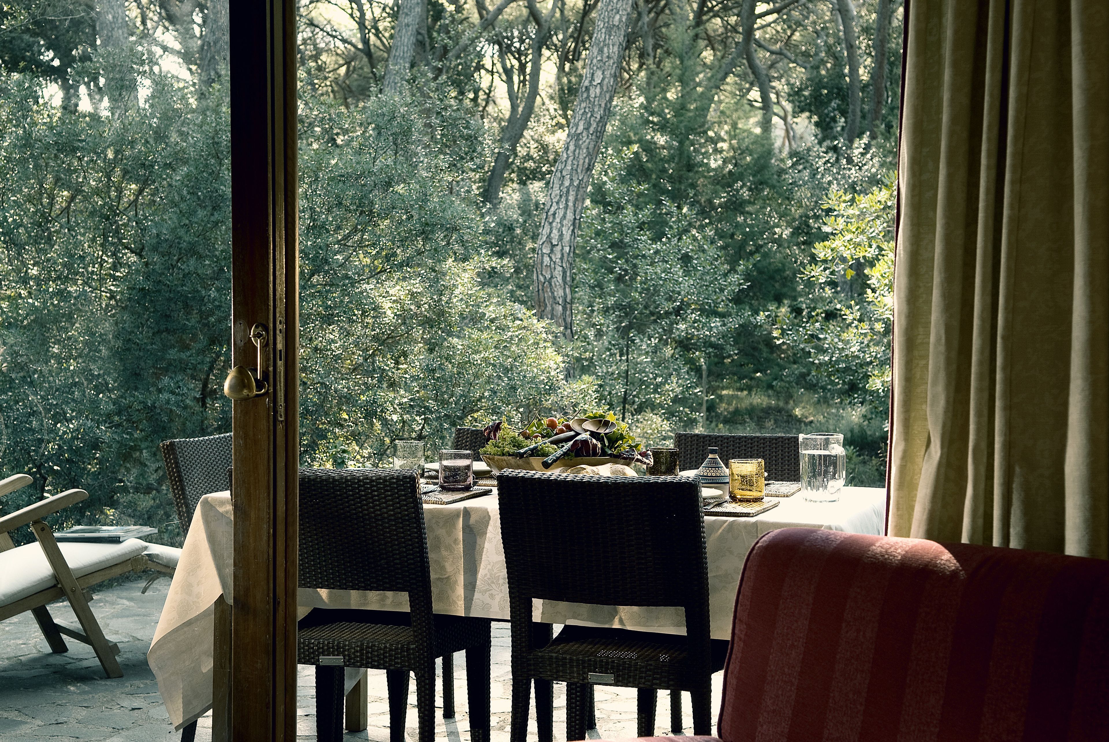 An outdoor dining area with wicker chairs and a table set for a meal, overlooking a forested area.