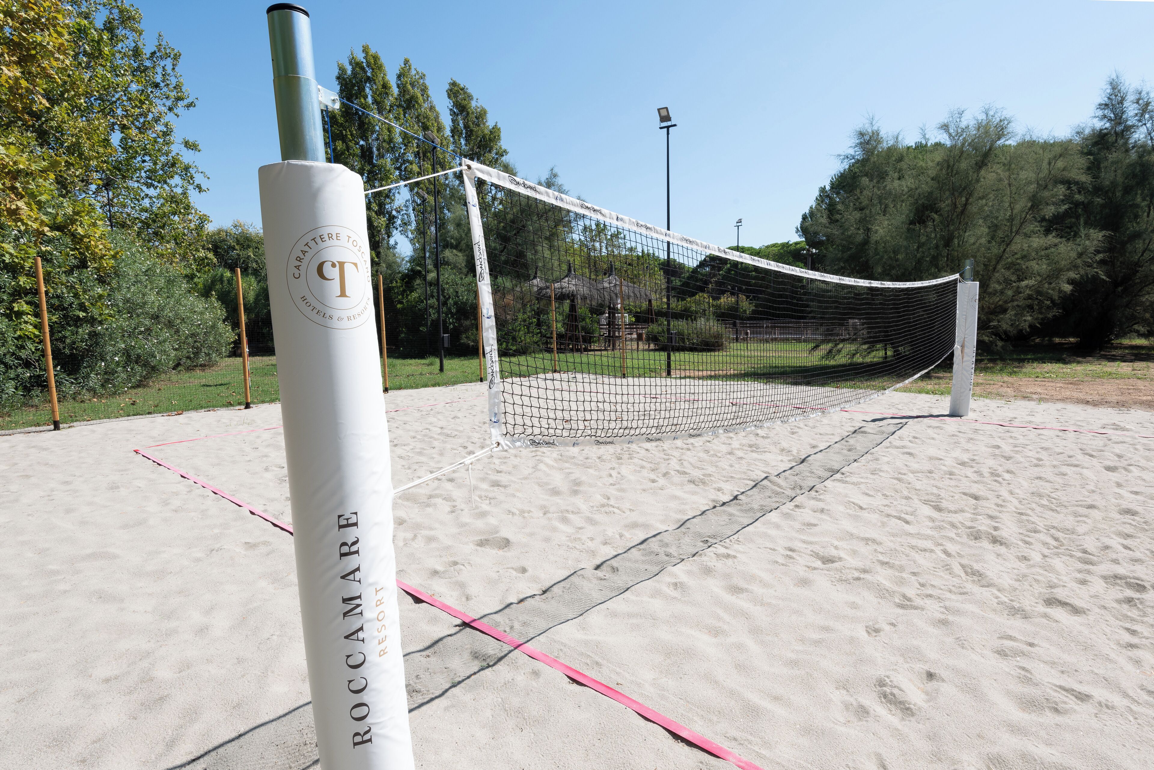 Una red de voleibol montada en una cancha de arena, con un poste de red que muestra la leyenda 'Carattere Toscane Hotels & Resorts'.