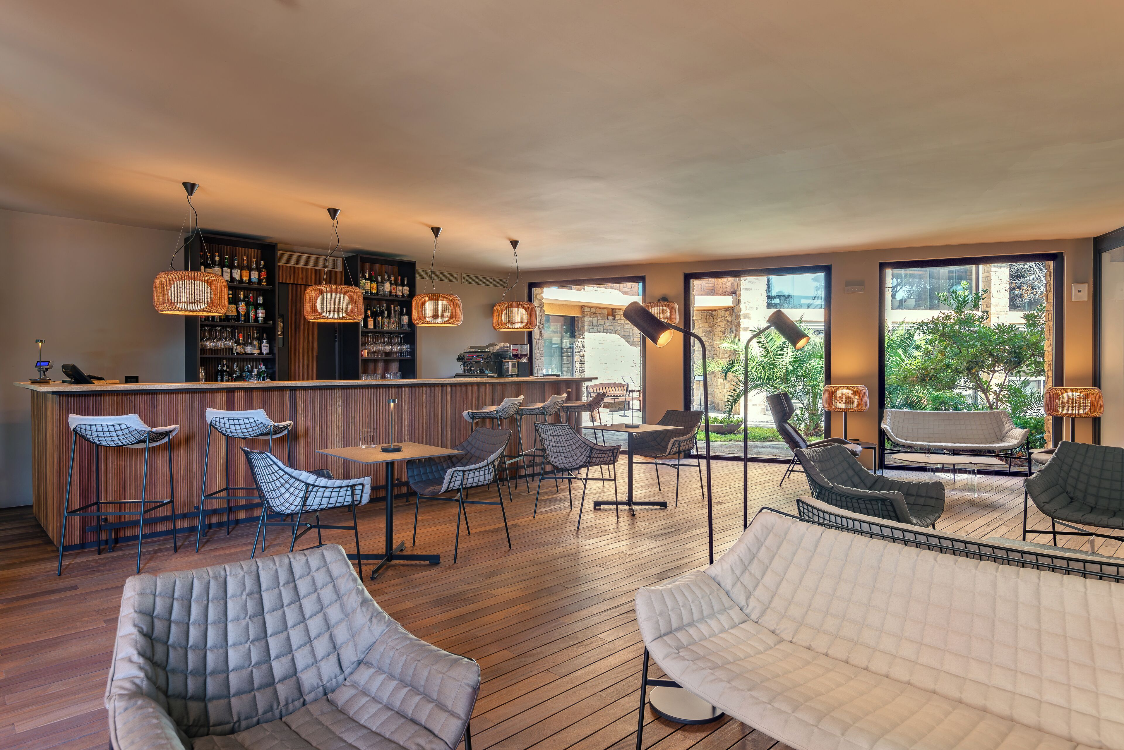 A bar area with wicker chairs, a wooden bar counter, and a view of the outdoors through large windows.