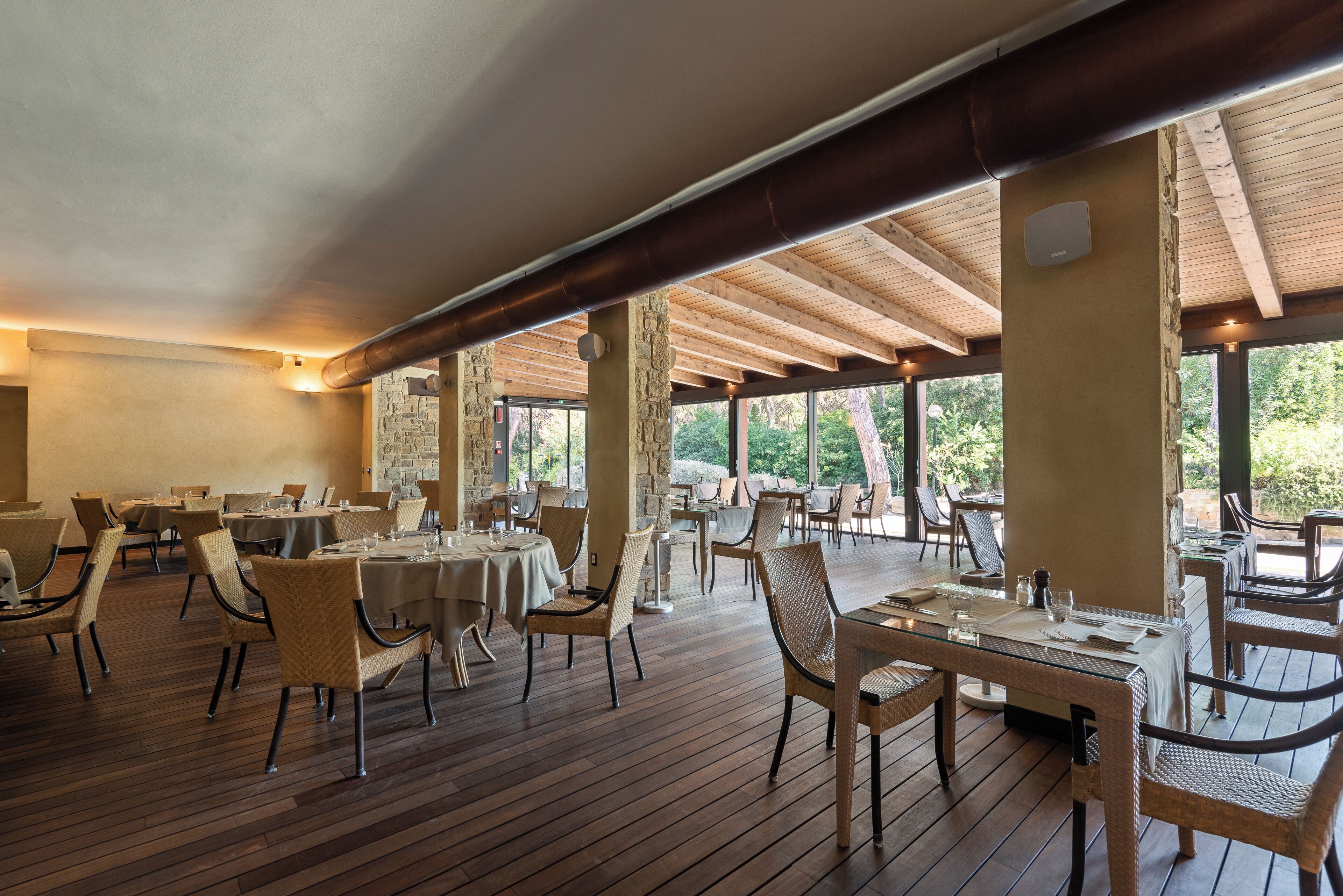 An indoor dining area with wooden flooring, tables, and wicker chairs.