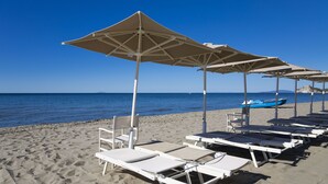 Ein Strand mit weißen Liegestühlen und beigen Sonnenschirmen.