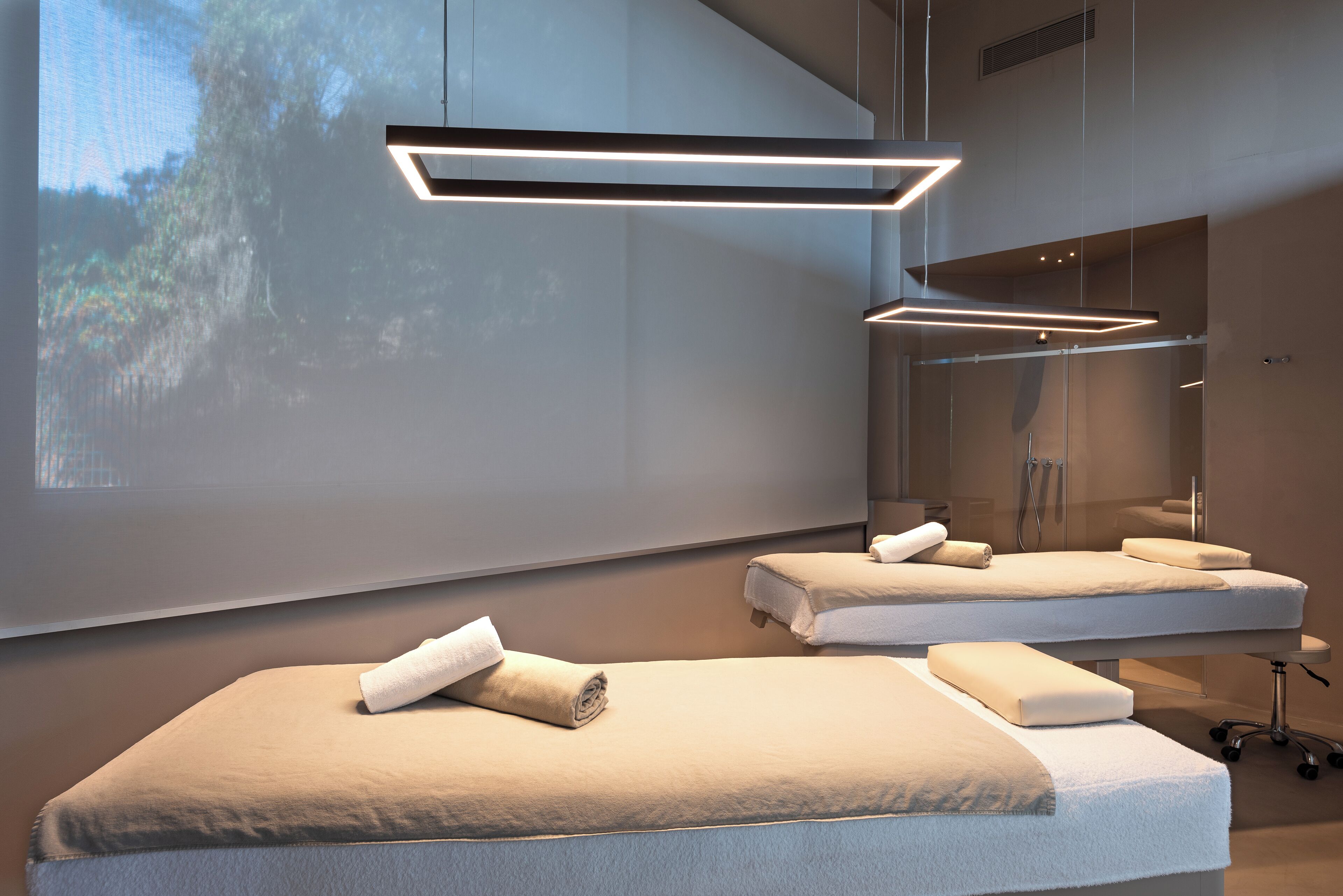 A modern spa room with two massage tables, each with a towel and a pillow.