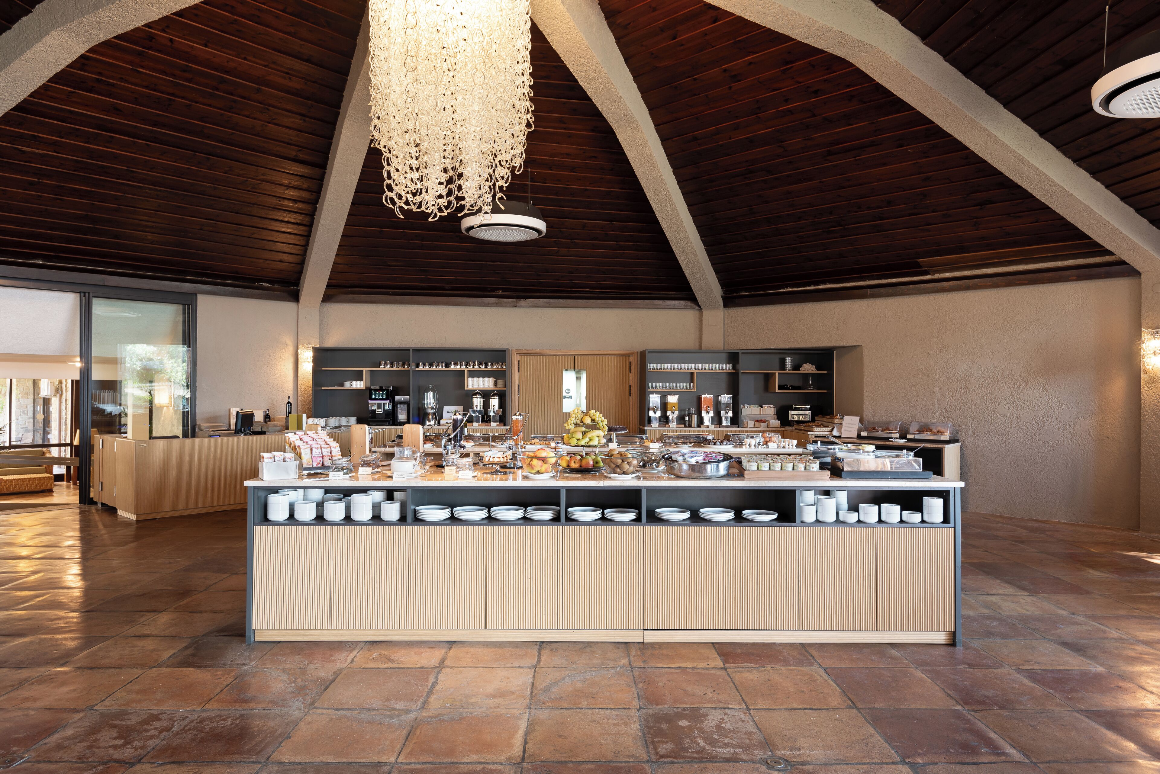 Um quarto espaçoso com teto alto, uma área de buffet central com diversos alimentos e uma cozinha moderna ao fundo.