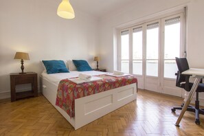 Un dormitorio con una cama, dos mesitas de noche con lámparas, un escritorio con una silla y un ventanal con vistas.