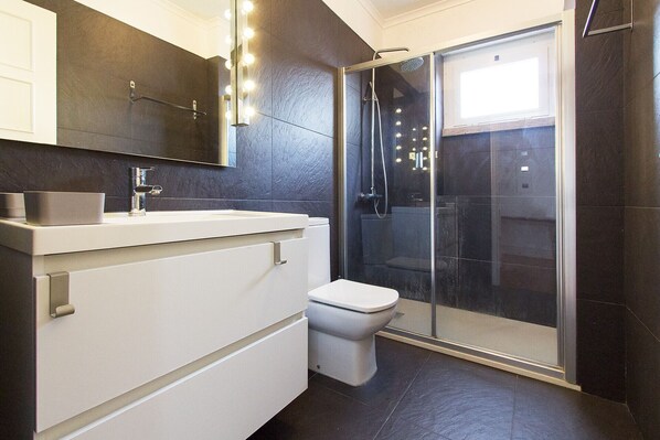Un baño moderno con ducha de vidrio, un lavamanos blanco y un inodoro.