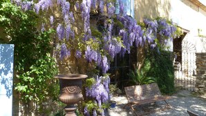 A garden with purple wisteria vines, a large urn, and a bench. - Mas du Puits d'Amour (Orange)