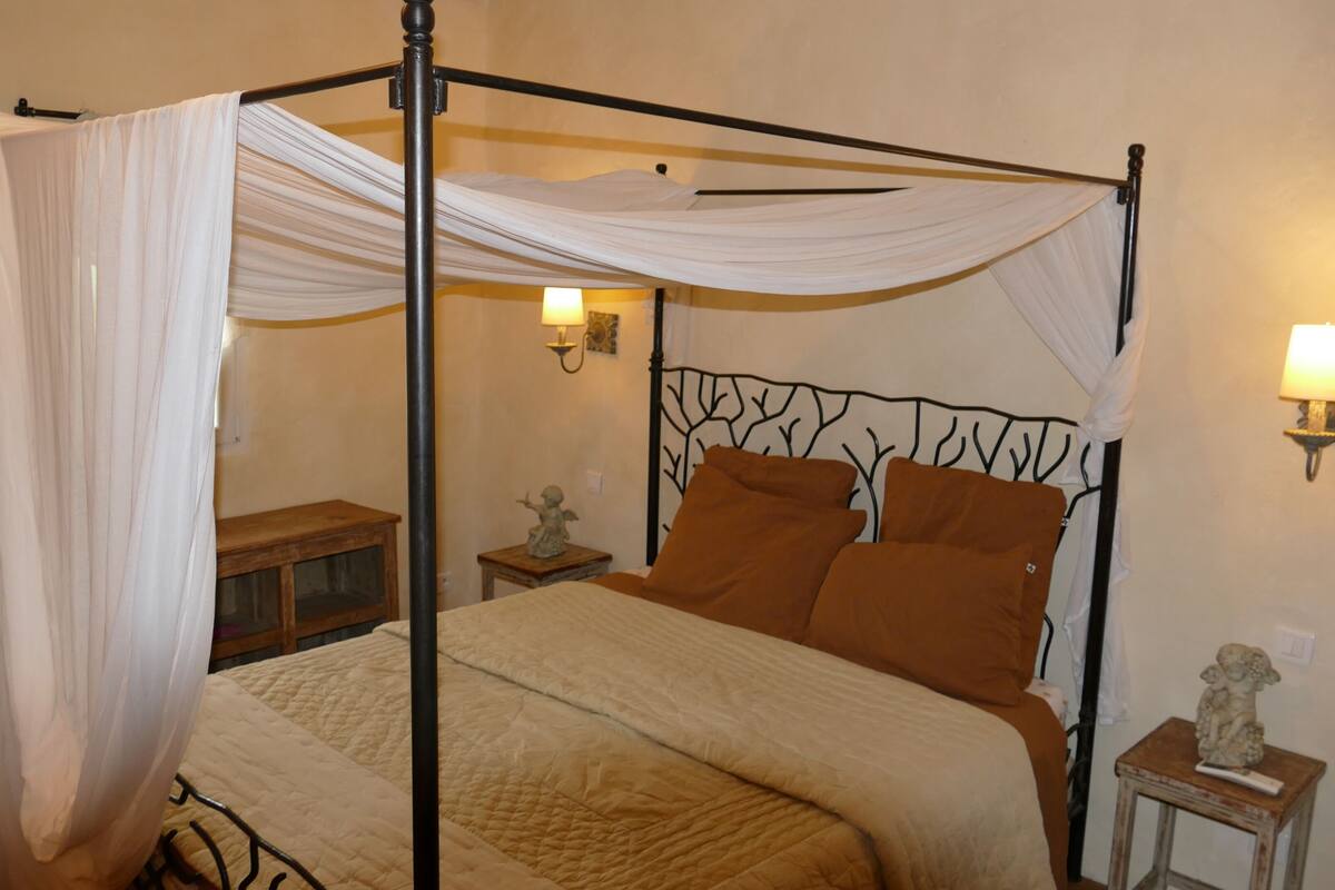 A four-poster bed with a canopy, two bedside lamps, and a nightstand with a statue.