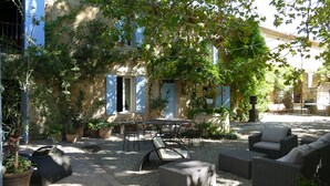 A courtyard with outdoor furniture, a table, and chairs. There are potted plants and a stone wall. - Mas du Puits d'Amour (Orange)