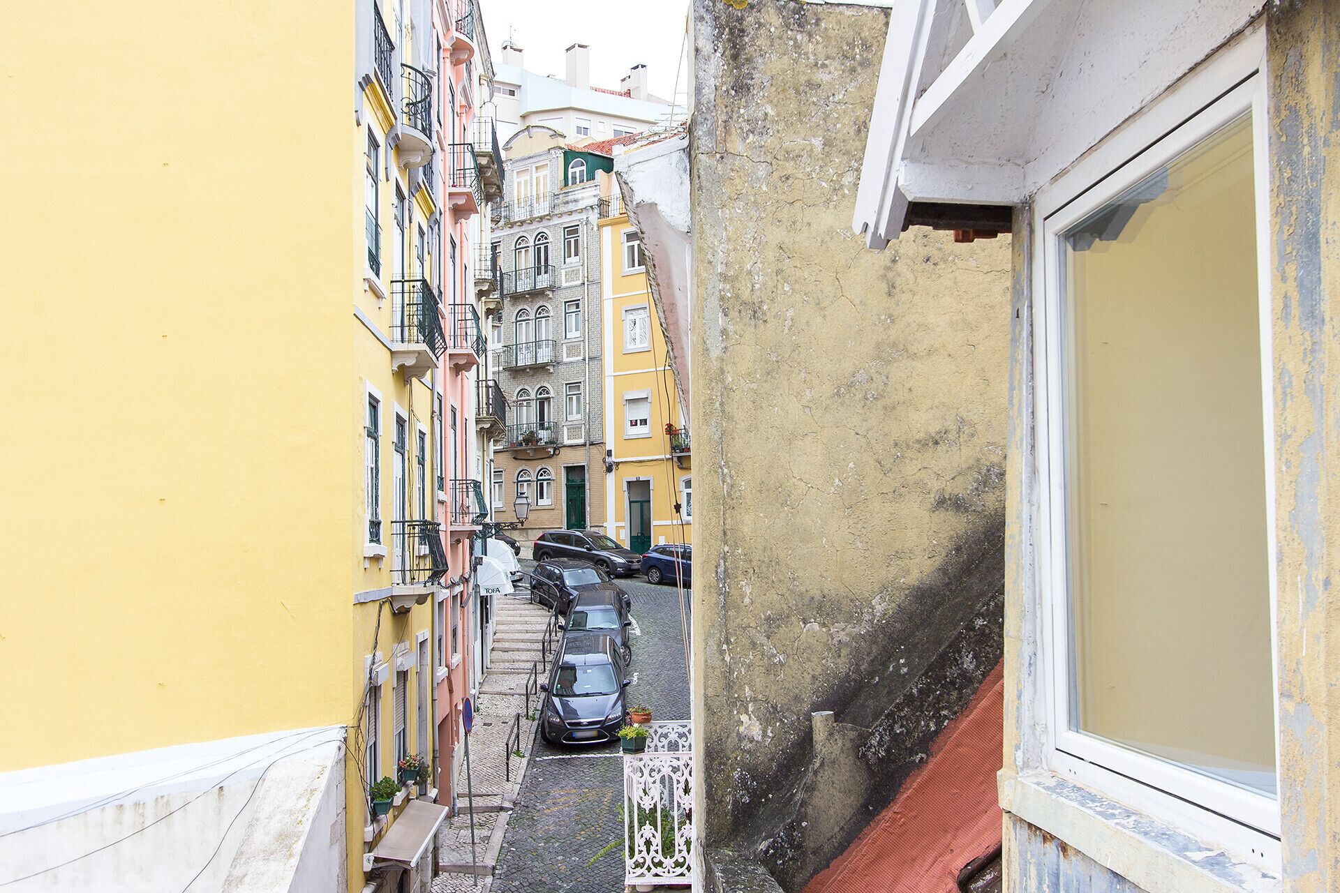 A narrow street with parked cars and buildings on both sides.