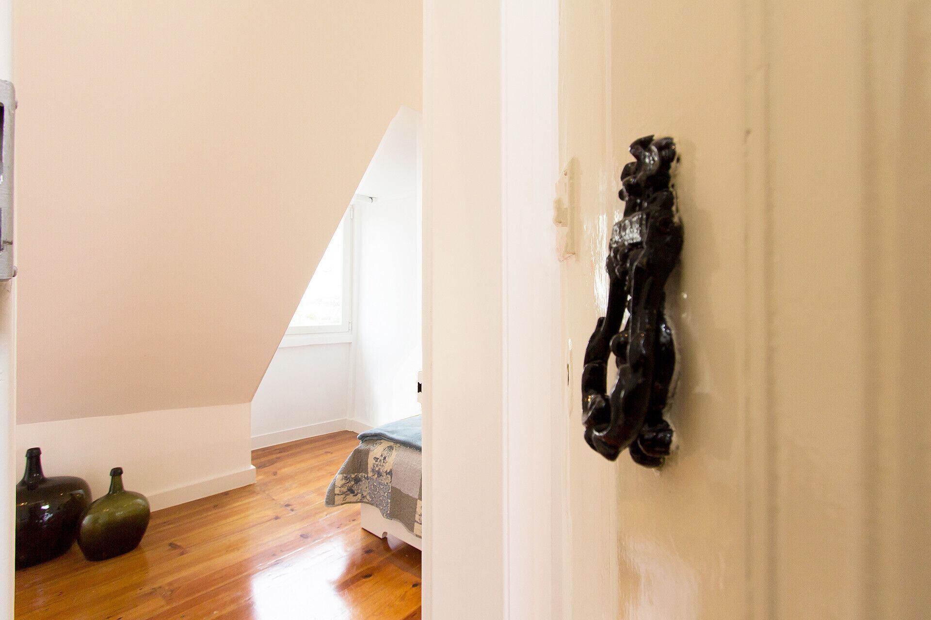 A room with a sloped ceiling, wooden flooring, and a white door with a black decorative element.