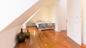 Un dormitorio con techo inclinado, cama con ropa de cama estampada, lámparas de noche y dos botellas en el suelo.