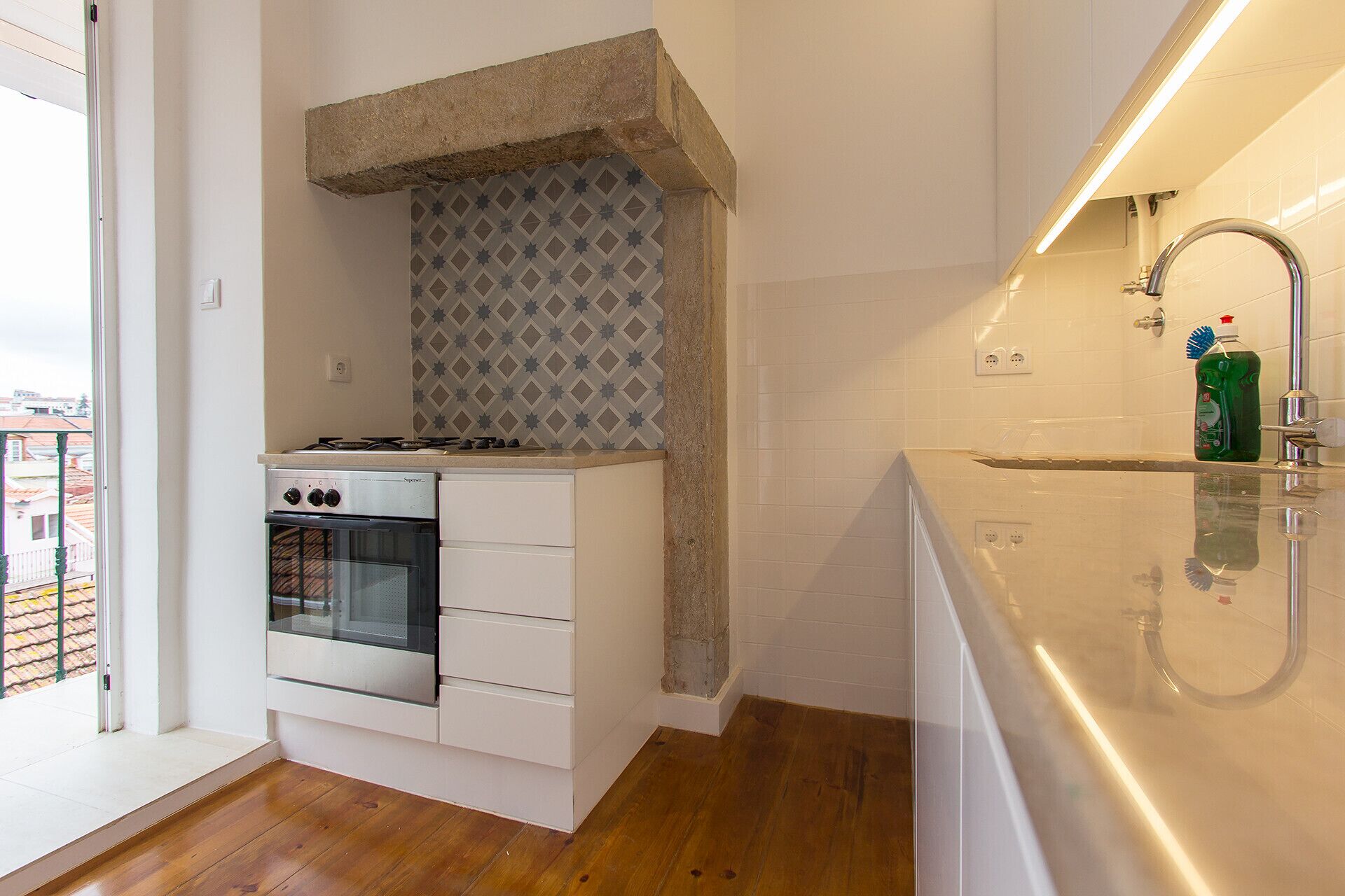 A modern kitchen with a built-in oven, a stainless steel sink, and a patterned backsplash.