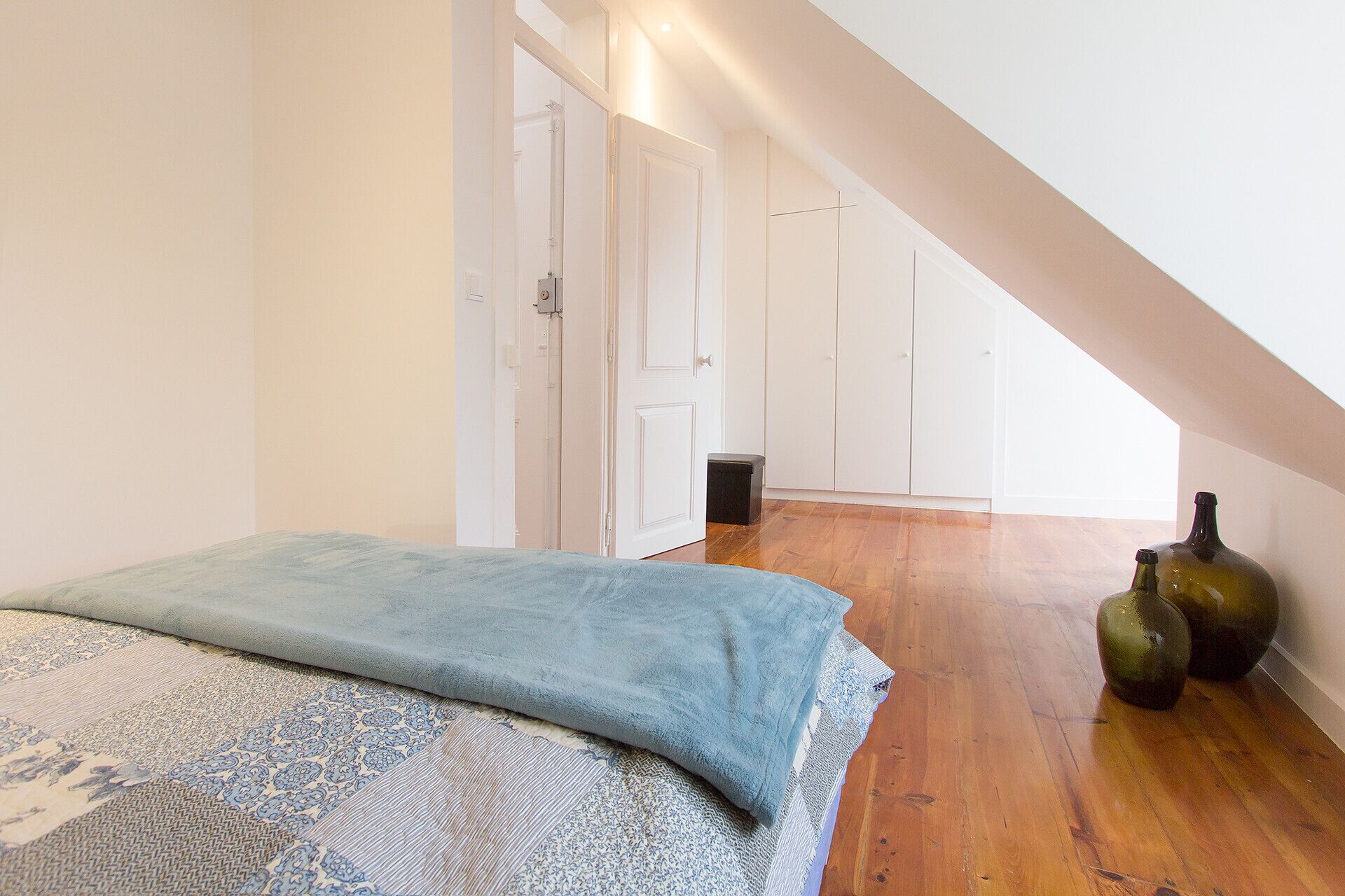 Une chambre à coucher avec un lit, un plancher en bois, une porte blanche et une bouteille par terre.
