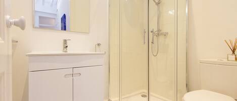 A modern bathroom with a glass-enclosed shower, a white sink, and a toilet.