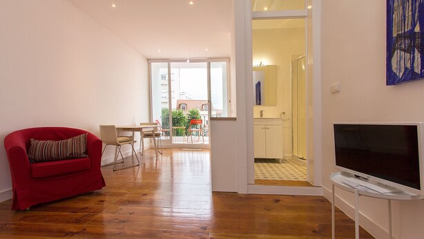 Un salón amplio con un sillón rojo, un televisor y una zona de comedor con mesa y sillas.