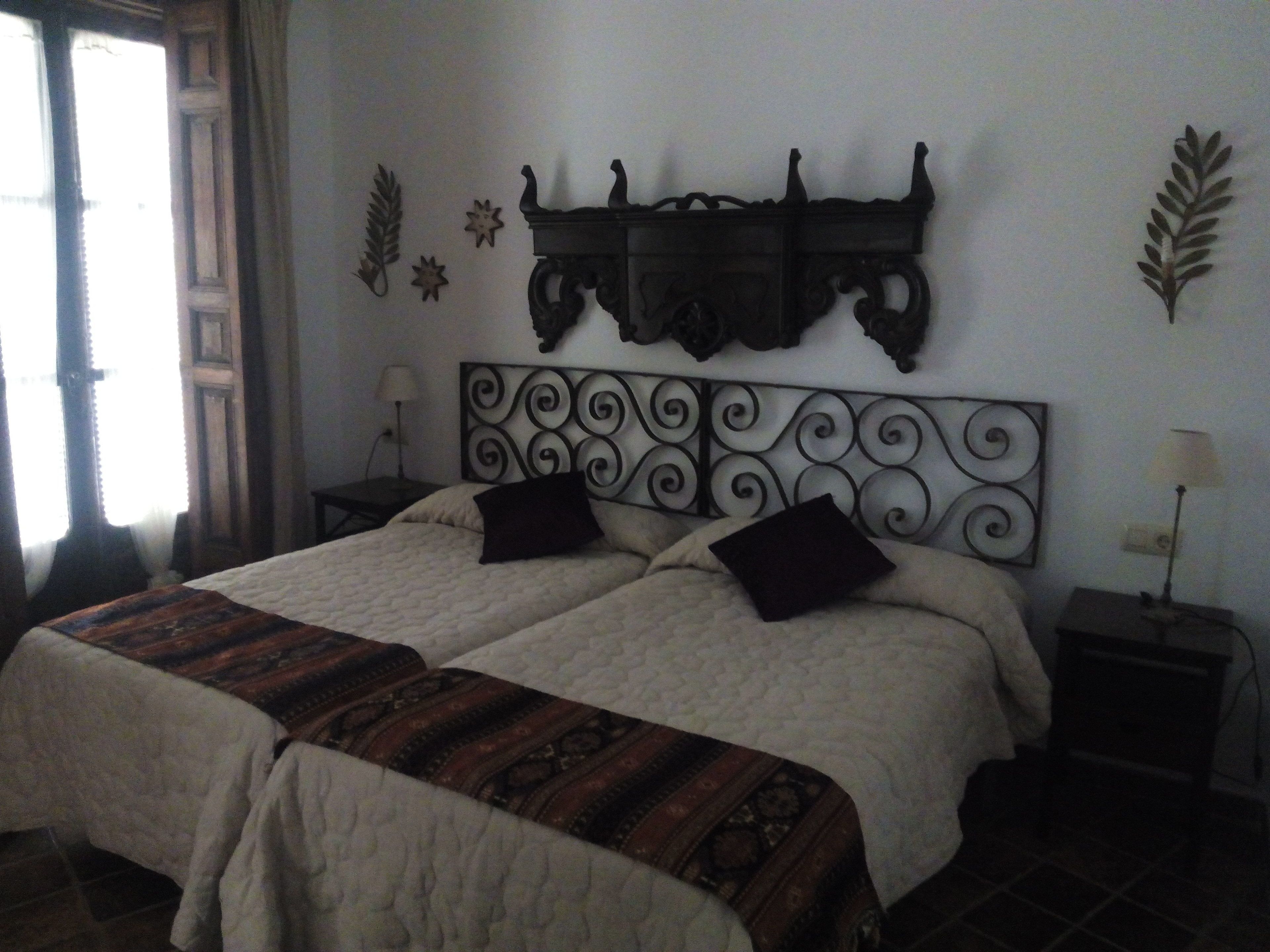 Una cama doble con un cabecero decorativo, dos mesitas de noche con lámparas y una ventana con cortinas.