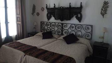 Una cama doble con un cabecero decorativo, dos mesitas de noche con lámparas y una ventana con cortinas.