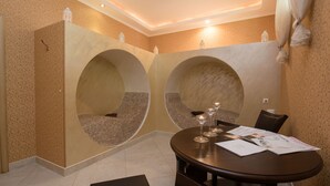 A dining area with a round table, two cushioned seating areas, and a patterned wall. - Apartments in Complex Poseidon (Nessebar)