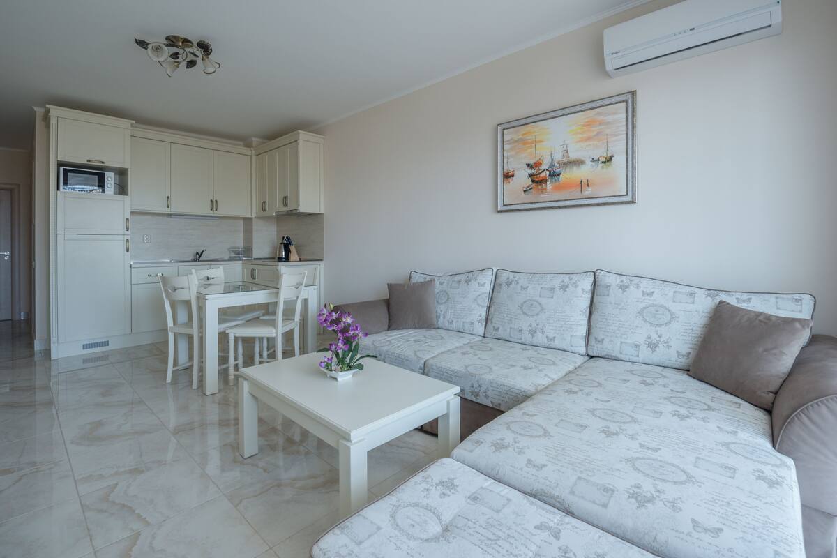 A modern living room with a sofa, a dining table, and a kitchen area.