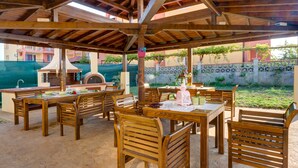 An outdoor patio with wooden tables and chairs, a brick oven, and a pergola structure. - Apartments in Complex Poseidon (Nessebar)