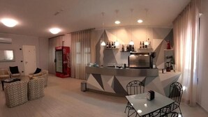 Una sala moderna con comedor, cocina equipada con refrigerador y cafetera, y zona de estar con dos sofás y una mesa de centro.