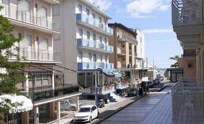 A street view with multi-story buildings, balconies, and a parked car. - Hotel Asso (Rimini)