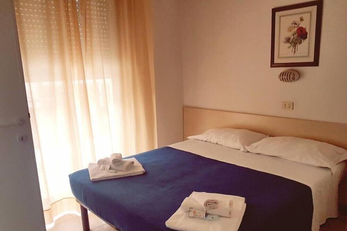 A hotel room with a bed, a window with curtains, a framed picture on the wall, and a small decorative item on the nightstand.