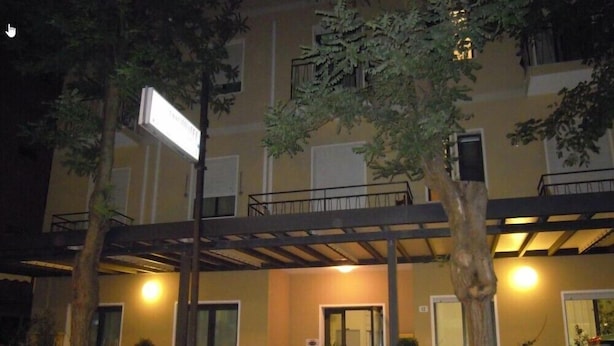 Un edificio de varios pisos con un balcón, plantas en macetas y un coche estacionado.