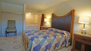 Ett hotellrum med en stor säng, en stol, ett nattduksbord, en lampa och ett badrum som syns genom en öppen dörr.