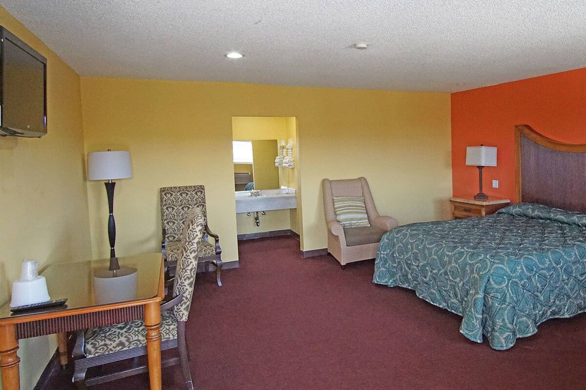 A hotel room with a bed, a chair, a desk, a lamp, a nightstand, and a mirror.