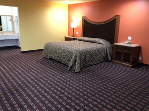Una habitación de hotel con cama, mesita de noche, lámpara y espejo.