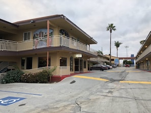 Un hotel de varios pisos con un balcón, un cartel que dice 'Lobby' y un estacionamiento con coches y una plaza reservada para discapacitados.