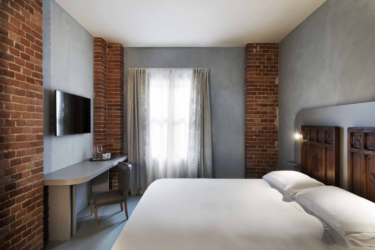 A hotel room with a bed, a desk, and a TV mounted on the wall.