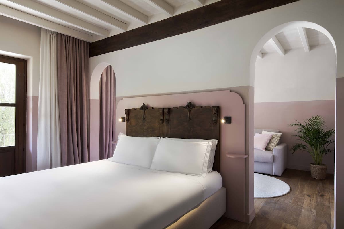 A bedroom with a large bed, a wooden headboard, a white sofa, a round rug, and a potted plant.